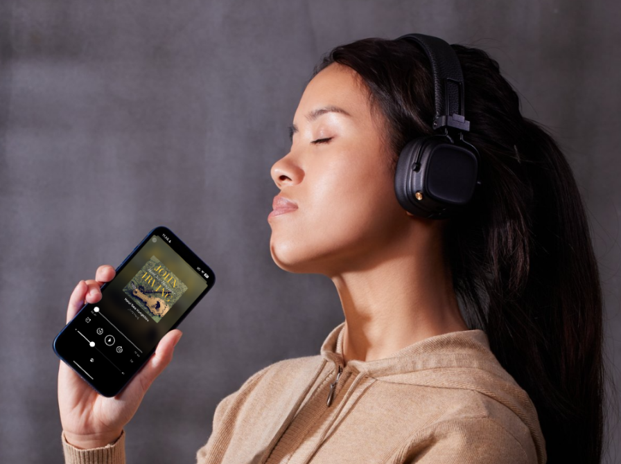 Kvinde der lytter til en lydbog med lukkede øjne, mens hun holder sin telefon i hånden