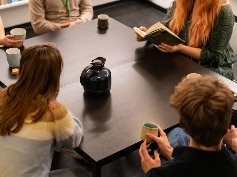 Gruppe af mennesker samlet om et bord med bog og kaffe